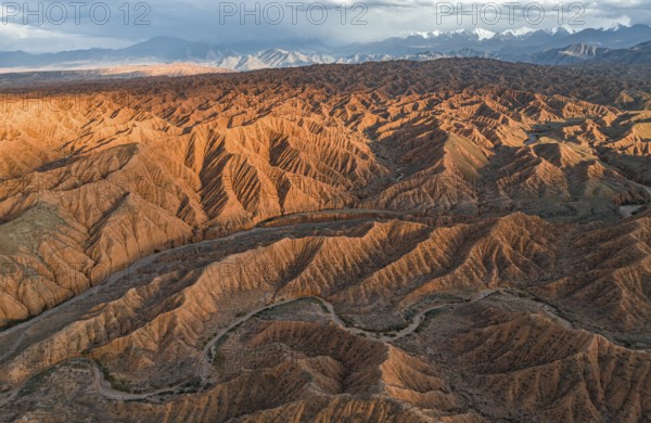 River bed runs through a landscape of eroded hills, badlands at sunset, mountain peaks of the Tian