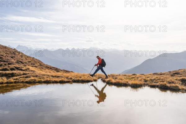 Mountaineer hiking with poles, reflected in a small mountain lake on the Krahberg, mountain