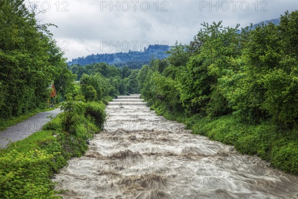 A river with a strong flow of water along a green landscape with wooded hills, Jenbach, Bad