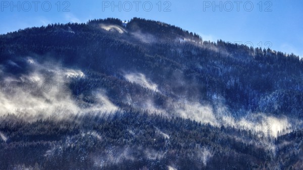 Misty mountains with snow and dense forests under a blue sky, Bad Feilnbach