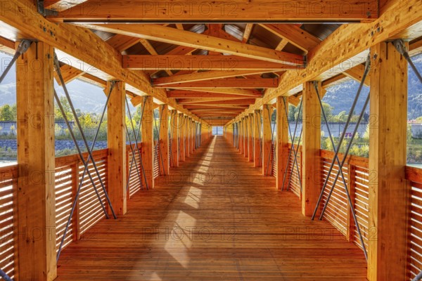 View along an illuminated wooden bridge with a view of the mountains and river, Inn footbridge,