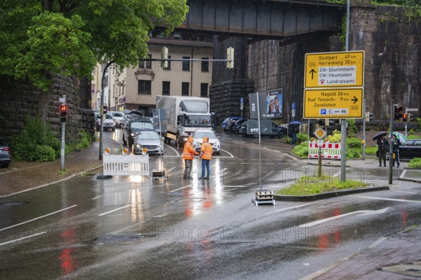 Road closure due to construction site in the city during rain, workers and traffic signs visible,