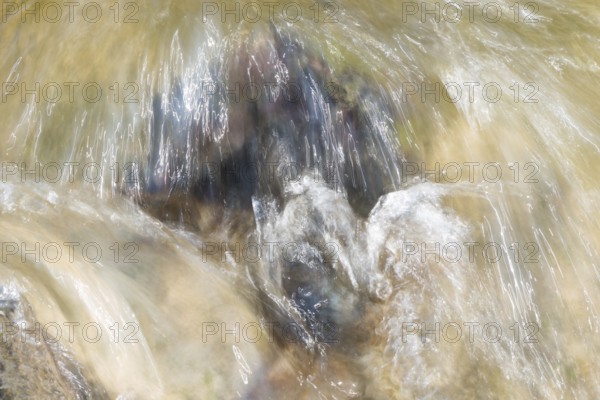 Moving water flows over a boulder, rapids, motion blur conveys the flow speed, reflections of the
