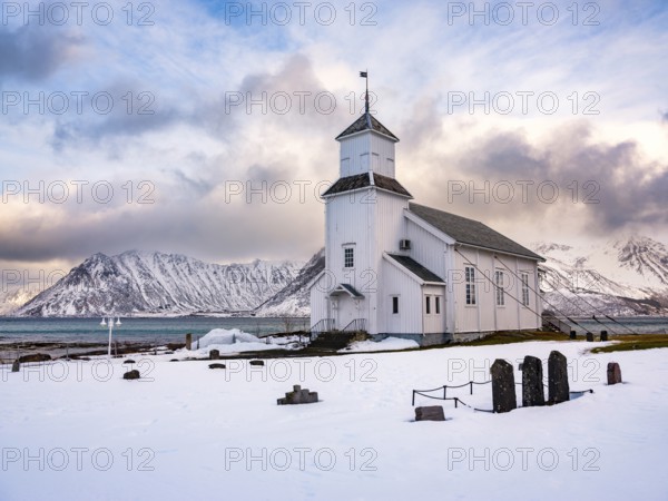 Gimsøy church with cemetery, snow-covered mountains in the background, winter, Gimsøya, Lofoten,