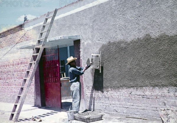 Construction worker throwing cement through a sieve to make wall panelling over modern red bricks,