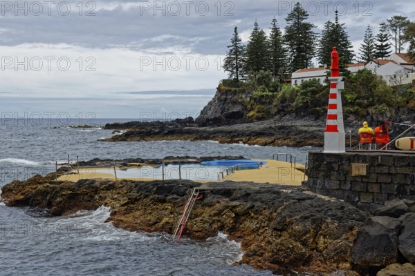 Small lighthouse and seawater swimming pool on the rocky coast under a cloudy sky, Caloura fishing