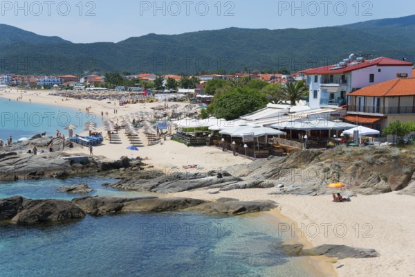 Beach with umbrellas and beach houses, clear blue water and mountains in the background, Sarti,