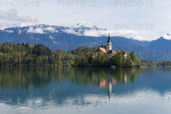 Church on an island, reflected in the calm lake, with mountain scenery in the background, Bled