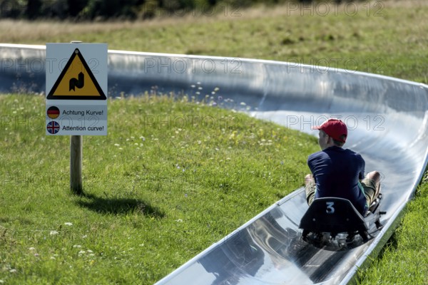 Boy with toboggan on the summer toboggan run, warning sign Attention curve, ski and toboggan arena,