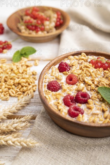 Wheat flakes porridge with milk, raspberry and currant in wooden bowl on white wooden background