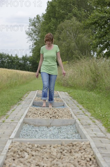 Woman walking barefoot over glass gravel and bottle corks, barefoot path Tilbeck Abbey, Havixbeck,