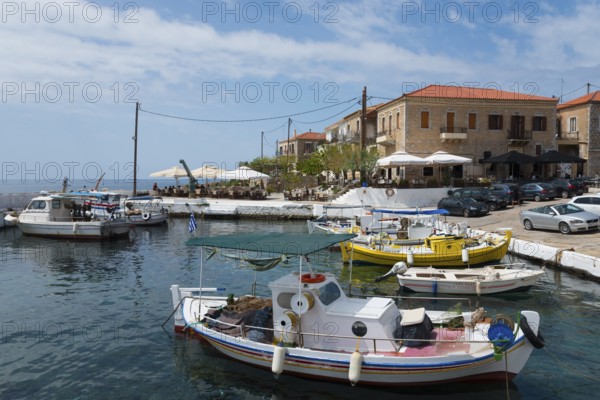 Colourful boats in the harbour next to a coastal town with umbrellas and old buildings, Agios