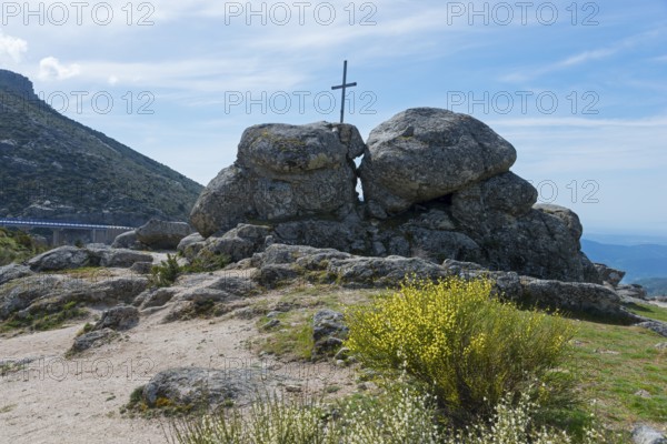 A cross stands between large rocks in a natural landscape under a sunny sky, at the Puerto del