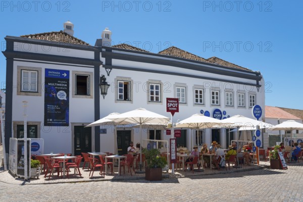 Café with umbrellas and guests outside in front of a blue-painted building on a sunny day, Faro