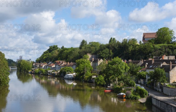Flusslandschaft mit Uferhäusern und üppigem Grün unter einem teilweise bewölkten Himmel, Nemours am