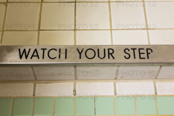 Top view of engraved Watch Your Step black lettering on chrome steel step of shower stall with