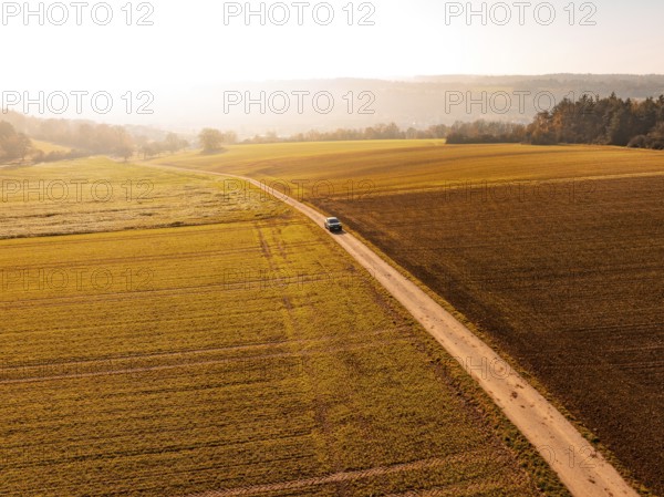 A car on a country lane, surrounded by wide, autumnal fields in soft light, electric car VW ID5,