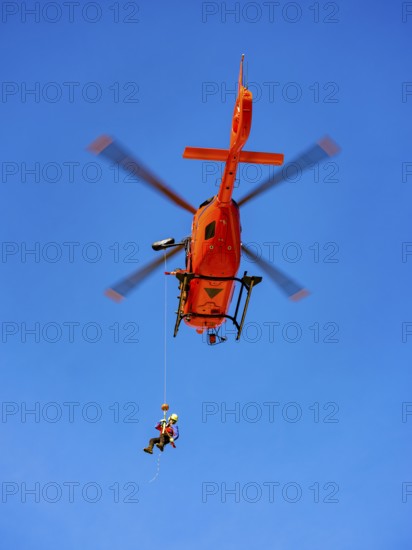 Mountain rescuer of the Bavarian Mountain Rescue Service being winched by the on-board mechanic of