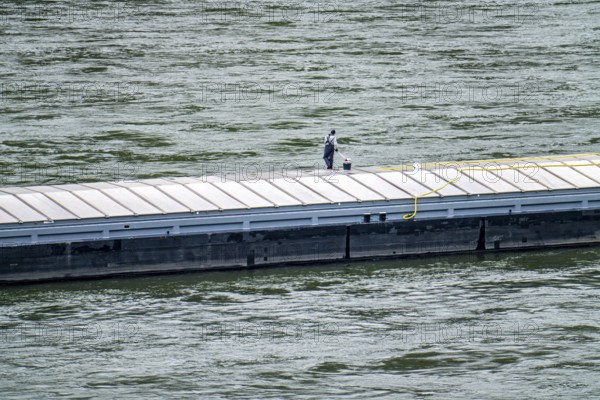 Inland waterway vessel, freighter, with closed cargo hatches, employee cleans the deck with water