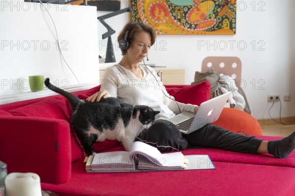 Woman, mid-50s, works from home, with laptop and communicates with colleagues via headset, home