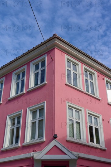 Historic building with pink facade and white window frames under a blue sky with light clouds,