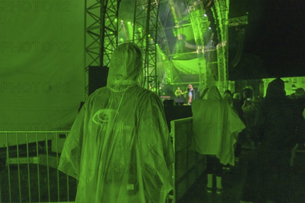 Person in green rain poncho at a night concert with green stage lighting, Klostersommer, Calw