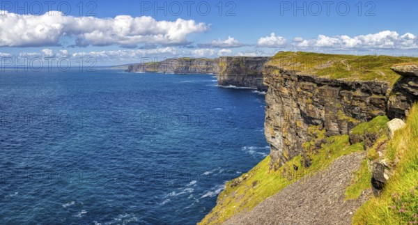 Sunlit cliffs on an endless blue coastline under a clear sky, Cliffs of Moher