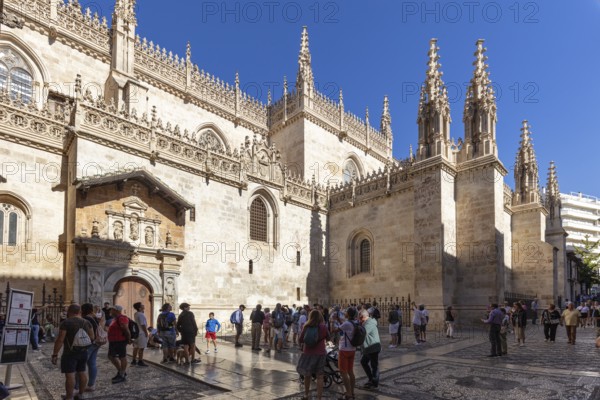 Gothic cathedral with elaborate decorations and tourists in the sunny inner courtyard, Granada