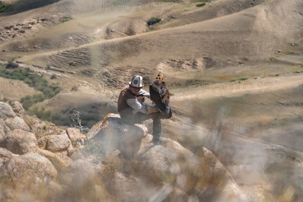 Traditional Kyrgyz eagle hunter hunting in the mountains in a dry landscape, near Kysyl-Suu, Issyk