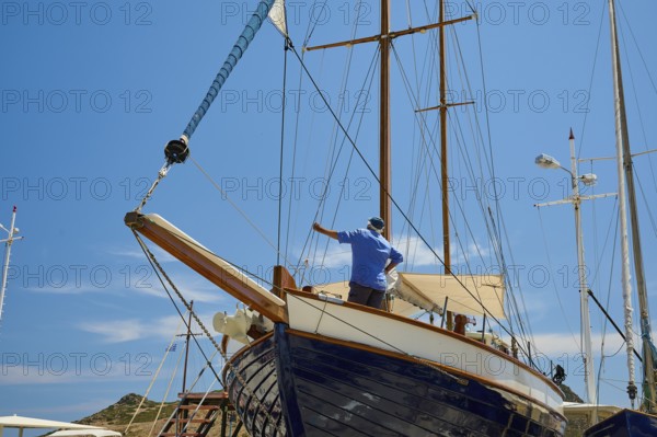 A man repairs the wooden sailing boat at the mast under a blue sky, Patmos Marine, boatyard,