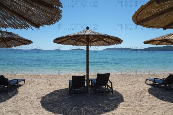 Sunny beach with deckchairs under straw umbrellas. Turquoise sea with islands in the background,
