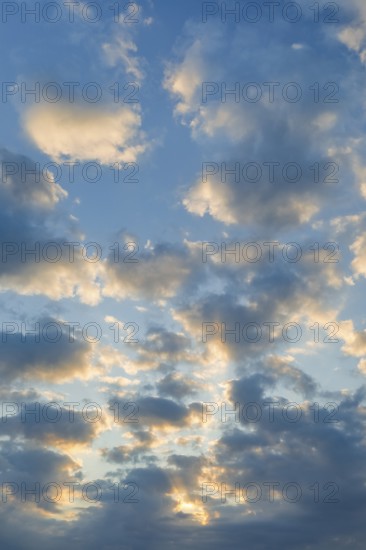 Sun breaks through cloud cover and illuminates fleecy clouds in the evening blue sky