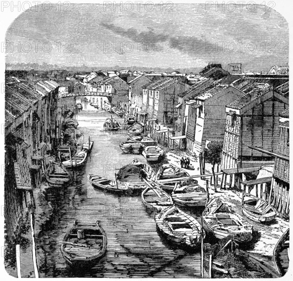 Wooden houses and sandy paths along a canal in old Tokyo, many rowing boats for transporting people