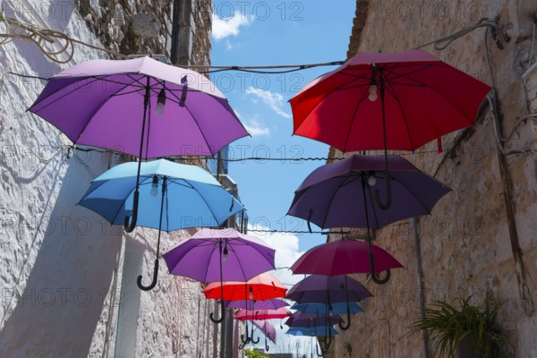 Colourful umbrellas hanging between old buildings under a clear blue sky, Old Town, Areopoli,