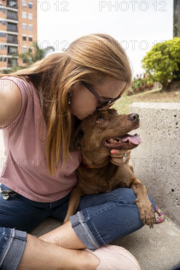 A affectionate woman hugs her pet, gives her dog a kiss on the forehead, and takes a photo