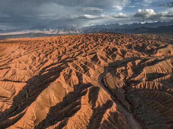 Landscape of eroded hills, badlands at sunset, mountain peaks of the Tian Shan Mountains in the