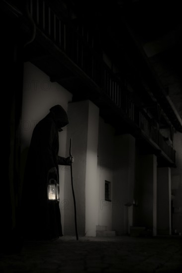Old man with hood, stick and lantern in gloomy city neighbourhood, Mindelheim, Unterallgäu,