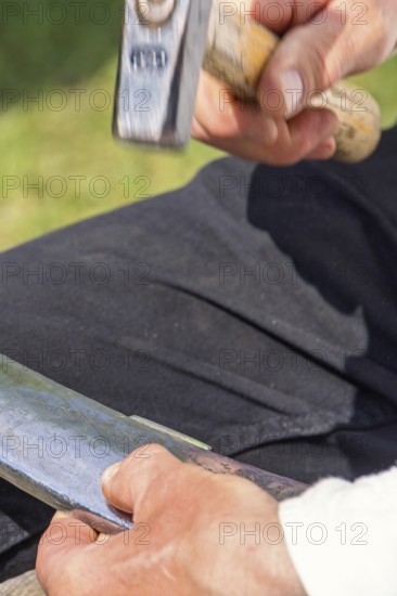 Man Peening a scythe blade using a hammer