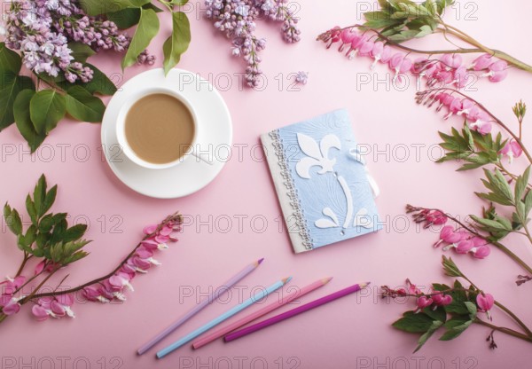 Purple lilac flowers and a cup of coffee with notebook and colored pencils on pastel pink