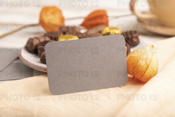 Gray business card with chocolate candies and physalis flowers on a white wooden background and