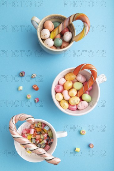 Heap of multicolored caramel candies in cups on blue pastel background. close up, top view, flat