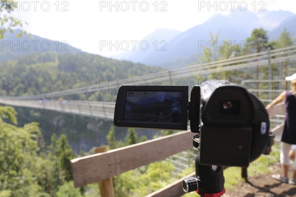 Close-up of a camcorder during video recording in nature. The mountains (Alps) and tourists can be