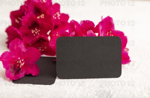 Black business card with purple azalea flowers on gray concrete background. side view, copy space,