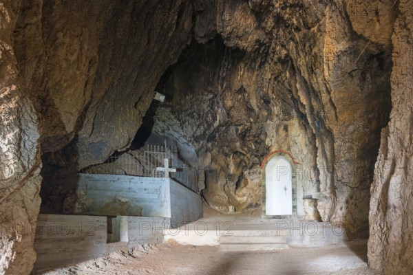 Interior view of a rocky cave with a tomb and a cross, a white niche visible, Church of Mary the