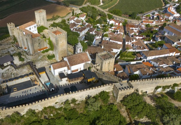Aerial view of a historic city with a castle and surrounding city walls, embedded in a hilly and