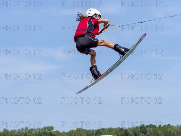 Boy or girl jumping with wakeboard, red life jacket, water sports, water skiing in wakepark