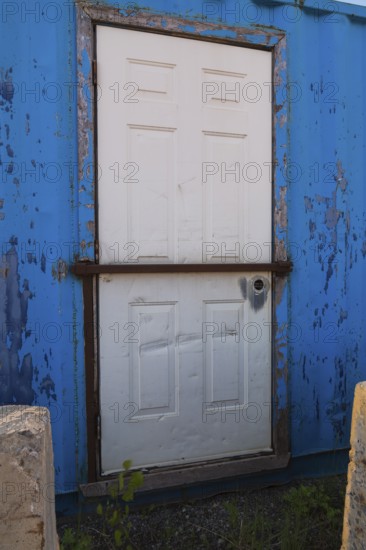Blue painted metal building with white entrance door protected with steel bar, Quebec, Canada,