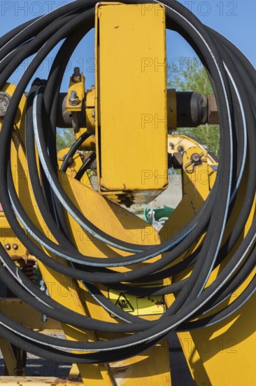 Coiled black rubber hose on yellow heavy machinery in junkyard, Quebec, Canada, North America