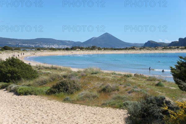 An idyllic beach with clear blue water and mountains in the background on a sunny day, Voidokilia