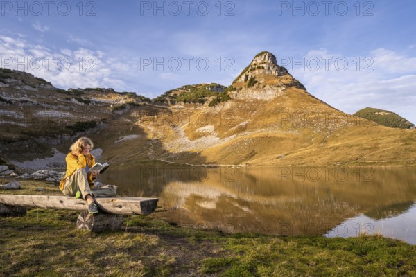 Lake Augstsee and the Atterkogel mountain on the Loser. A hiker sits on a bench and reads a book.